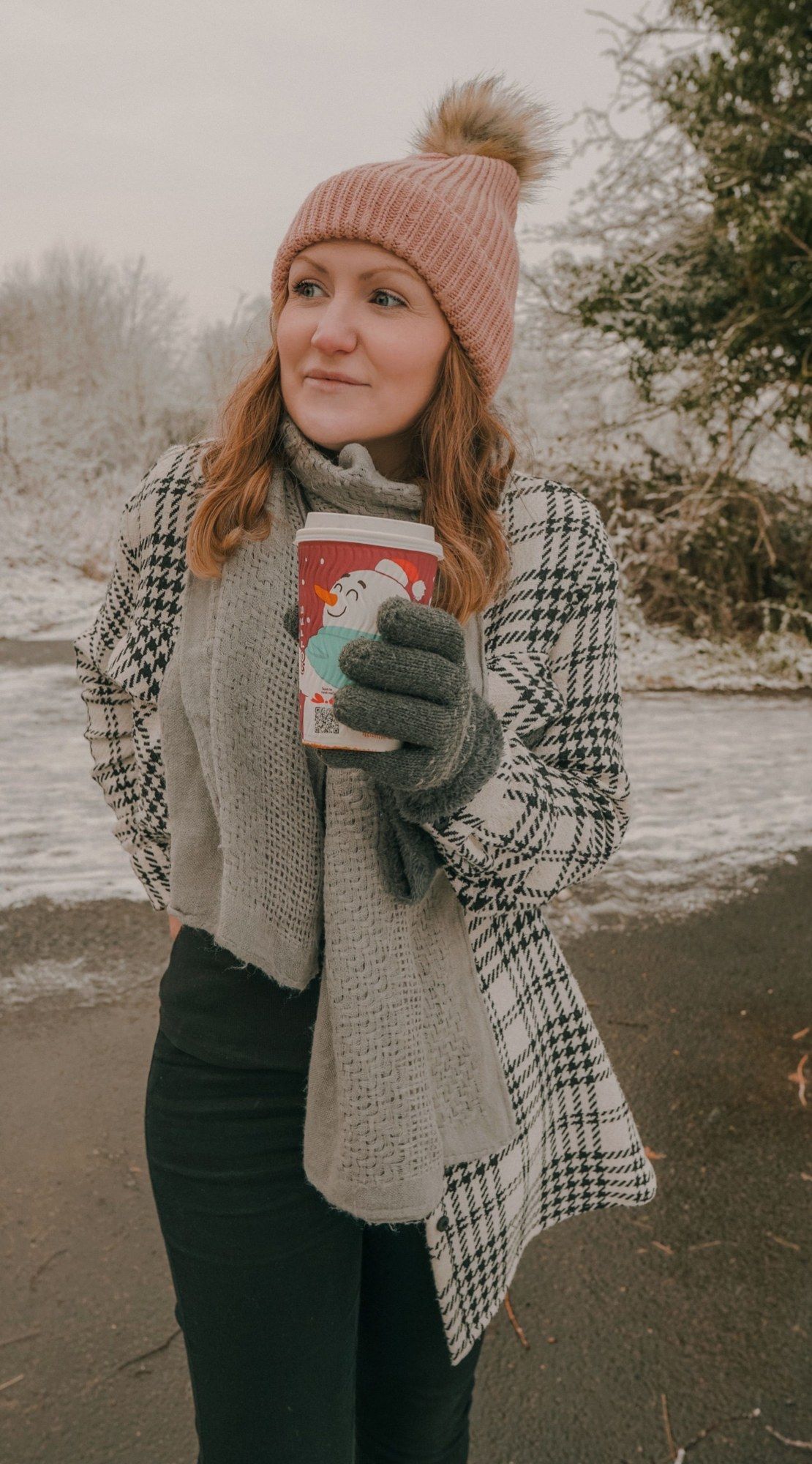 Mujer con gorro y bufanda sosteniendo una taza en un ambiente invernal